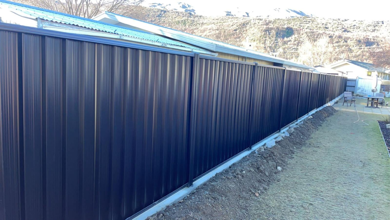 Long run of dark colour panel fencing along a property boundary, Central Otago