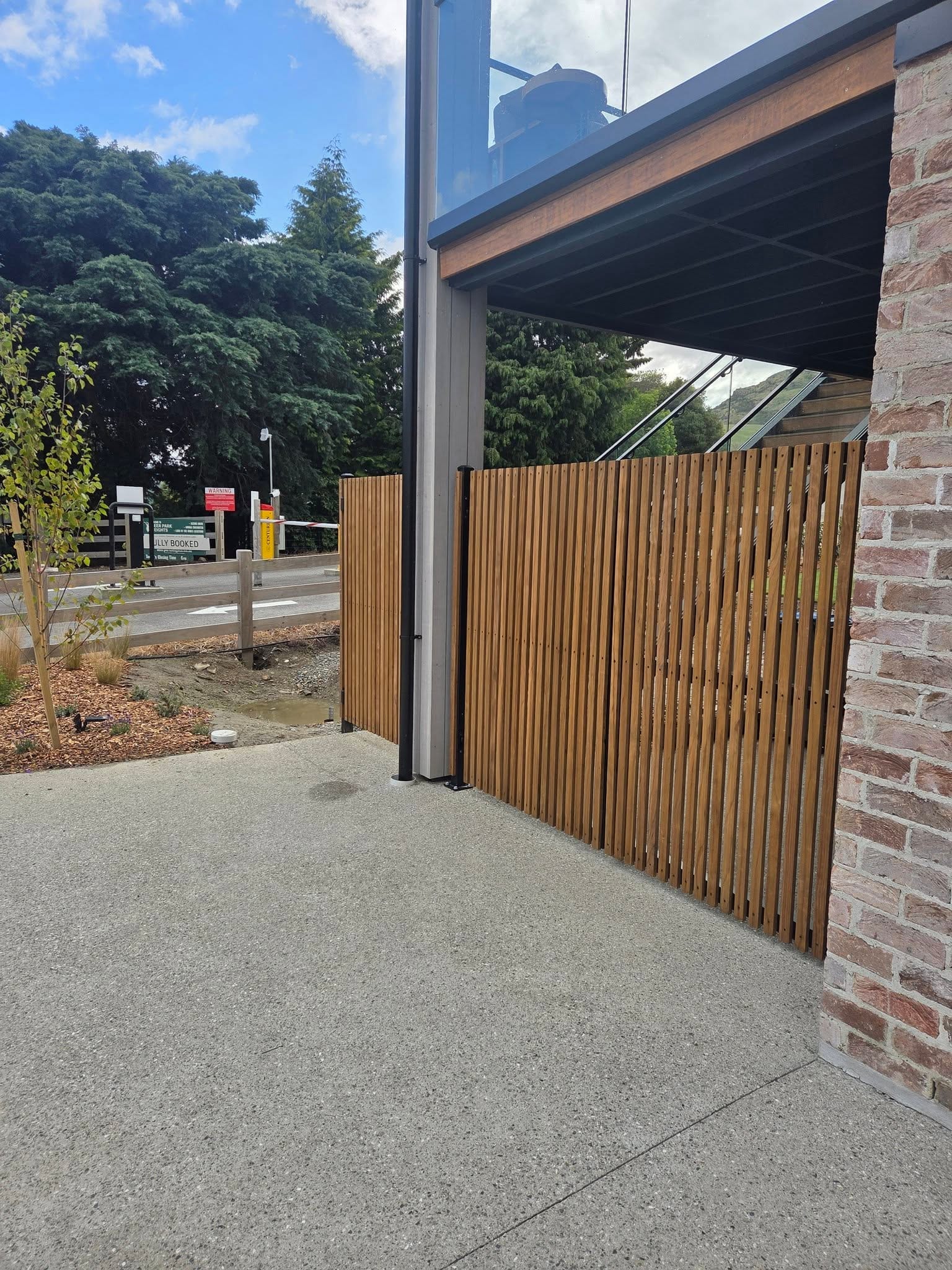 Vertical cedar timber slat fence panel beside a modern brick and glass building, Queenstown