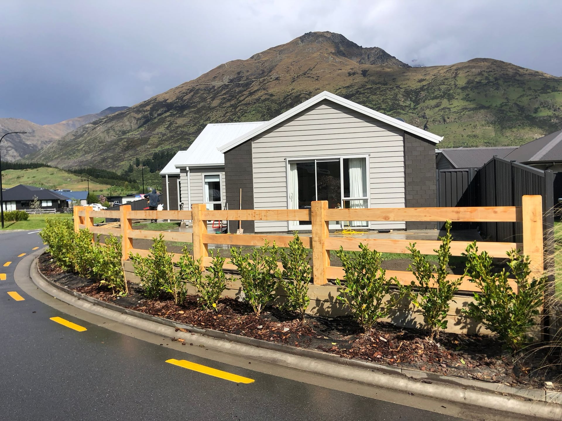 Macrocarpa post and rail fence along a street with mountain backdrop, Queenstown