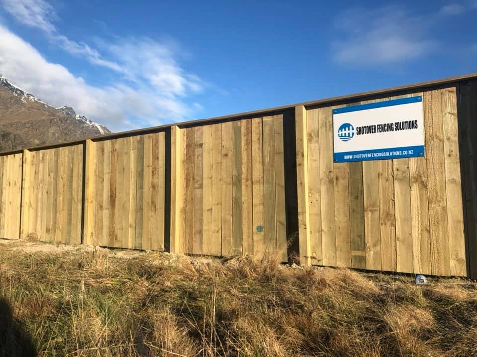 Pine paling fence with Shotover Fencing signage and snow-covered Remarkables, Queenstown