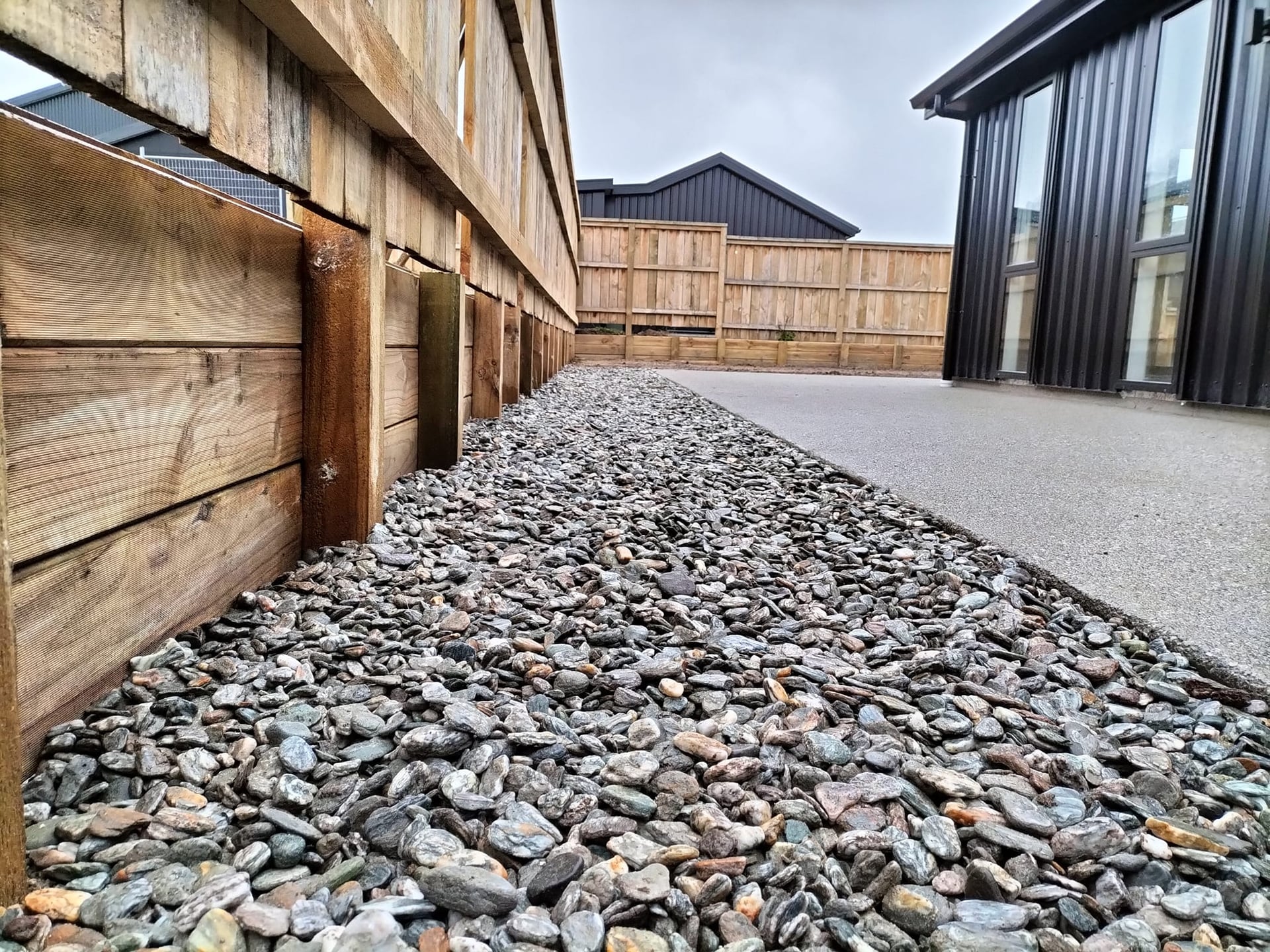 Low-angle view of timber sleeper retaining wall beside gravel driveway, Queenstown